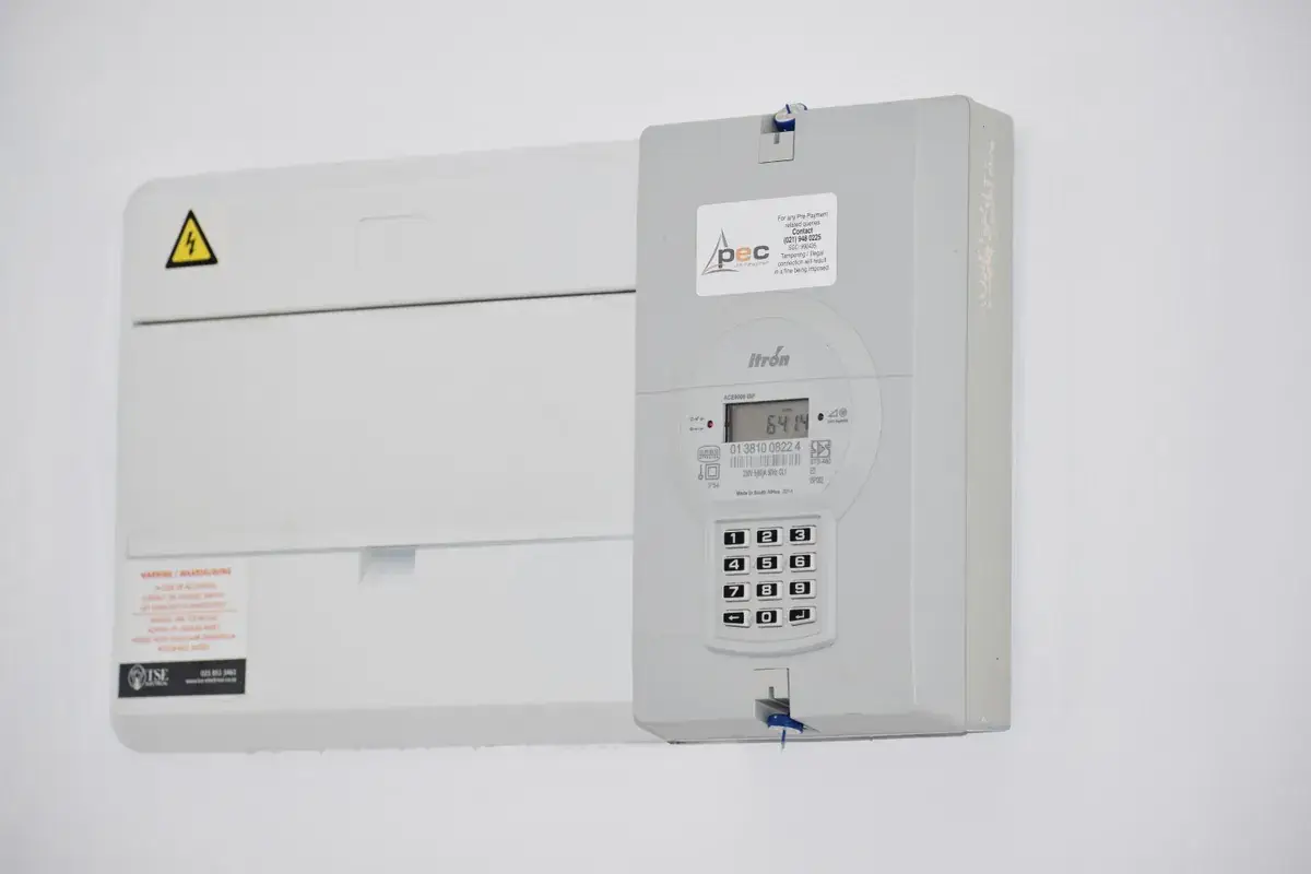 Digital prepayment electricity meter and consumer unit mounted on a plain white wall