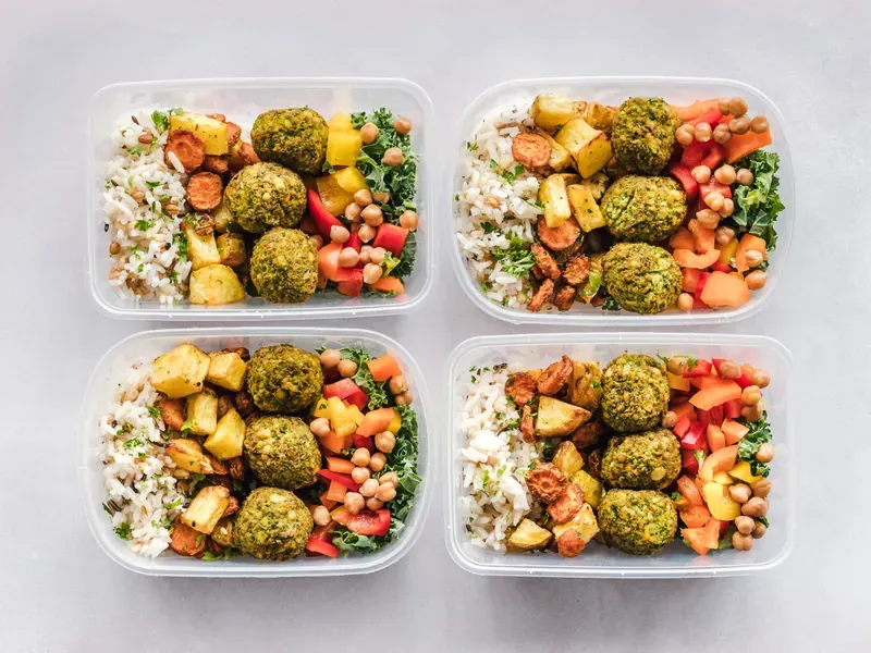 Four identical plastic meal-prep boxes, each packed with rice, falafel, chickpeas and roasted vegetables