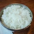 Steel bowl of plain white rice on a dark wooden table beside a folded paper napkin