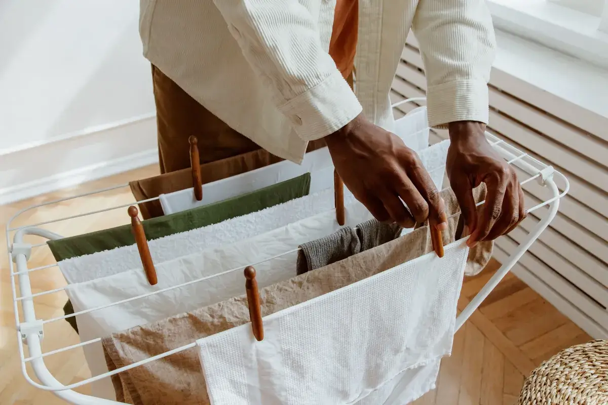 Hands pegging folded towels and linen onto a white concertina airer beside a radiator