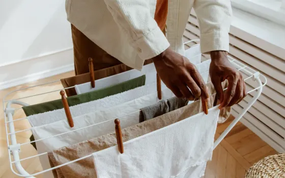 Hands pegging folded towels and linen onto a white concertina airer beside a radiator