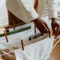 Hands pegging folded towels and linen onto a white concertina airer beside a radiator