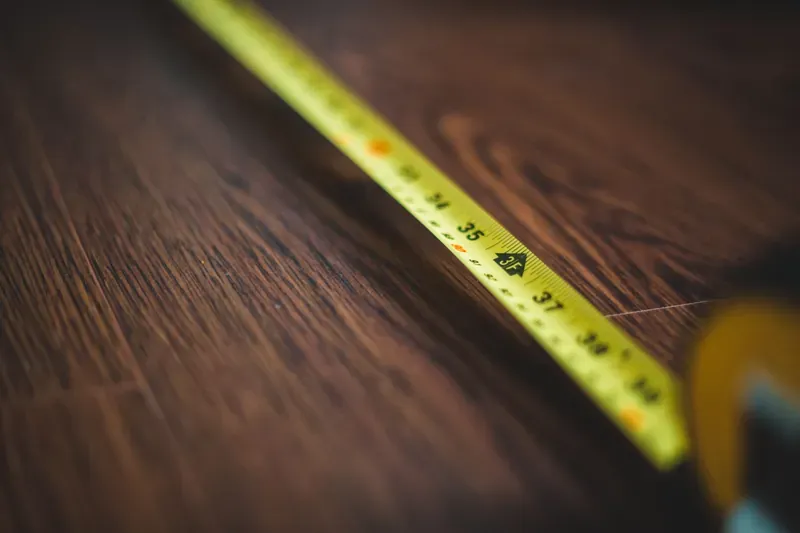 Close-up of a yellow tape measure stretched diagonally across dark wooden floorboards, with cm markings visible