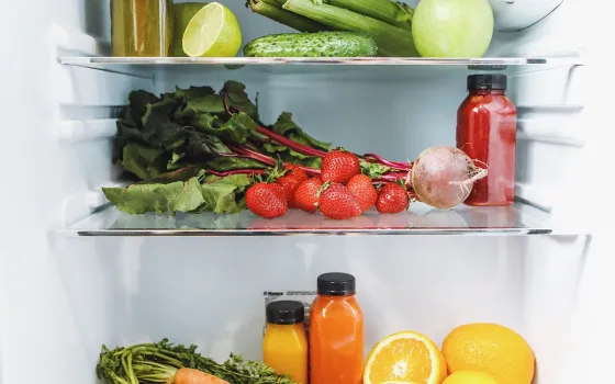 Open fridge shelves packed with strawberries, beetroot, cucumber, celery, citrus and fresh juice bottles