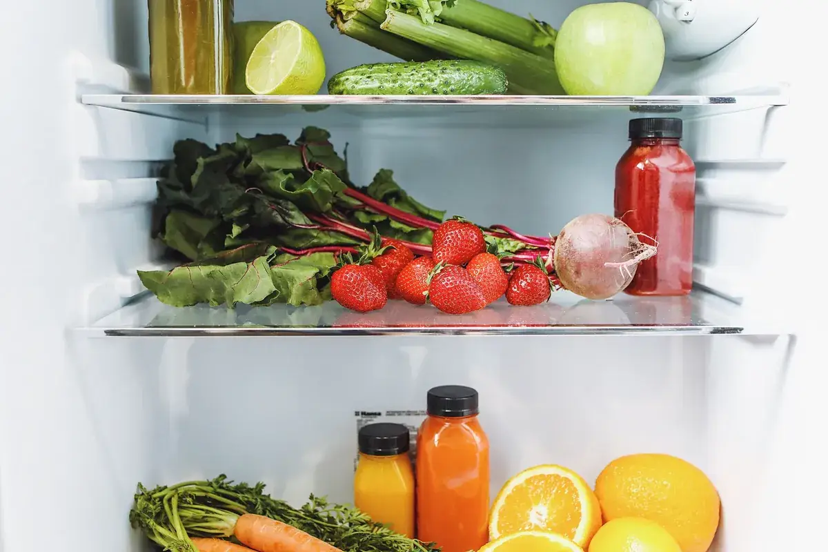 Open fridge shelves packed with strawberries, beetroot, cucumber, celery, citrus and fresh juice bottles