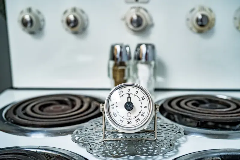 Close-up of an analogue kitchen timer with a white dial, standing on a vintage gas stove top