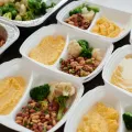 Rows of white meal-prep containers holding beans, broccoli, cauliflower and mashed squash