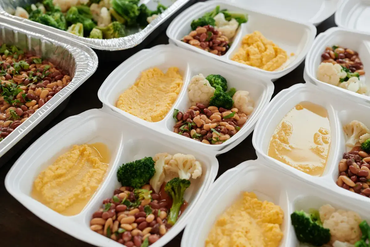 Rows of white meal-prep containers holding beans, broccoli, cauliflower and mashed squash