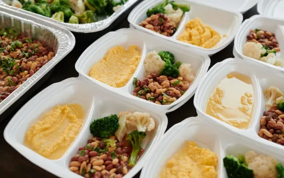 Rows of white meal-prep containers holding beans, broccoli, cauliflower and mashed squash
