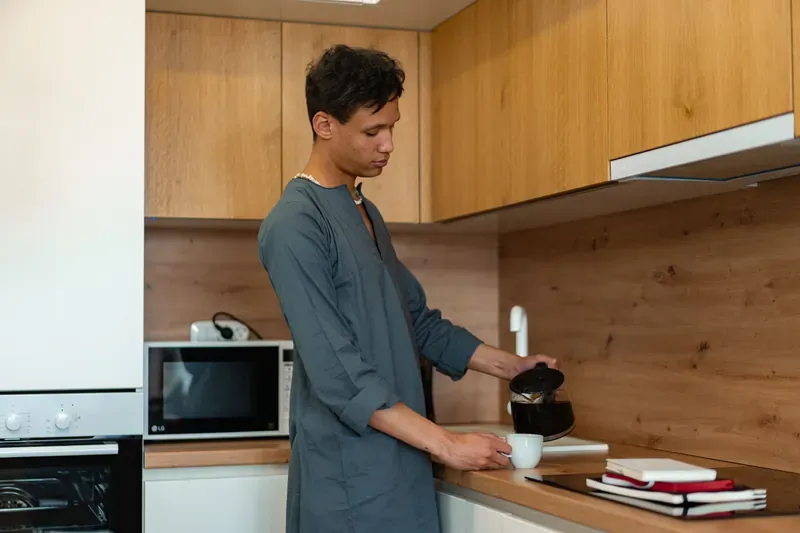 Man pouring coffee in a kitchen, with a kettle visible on the worktop behind him